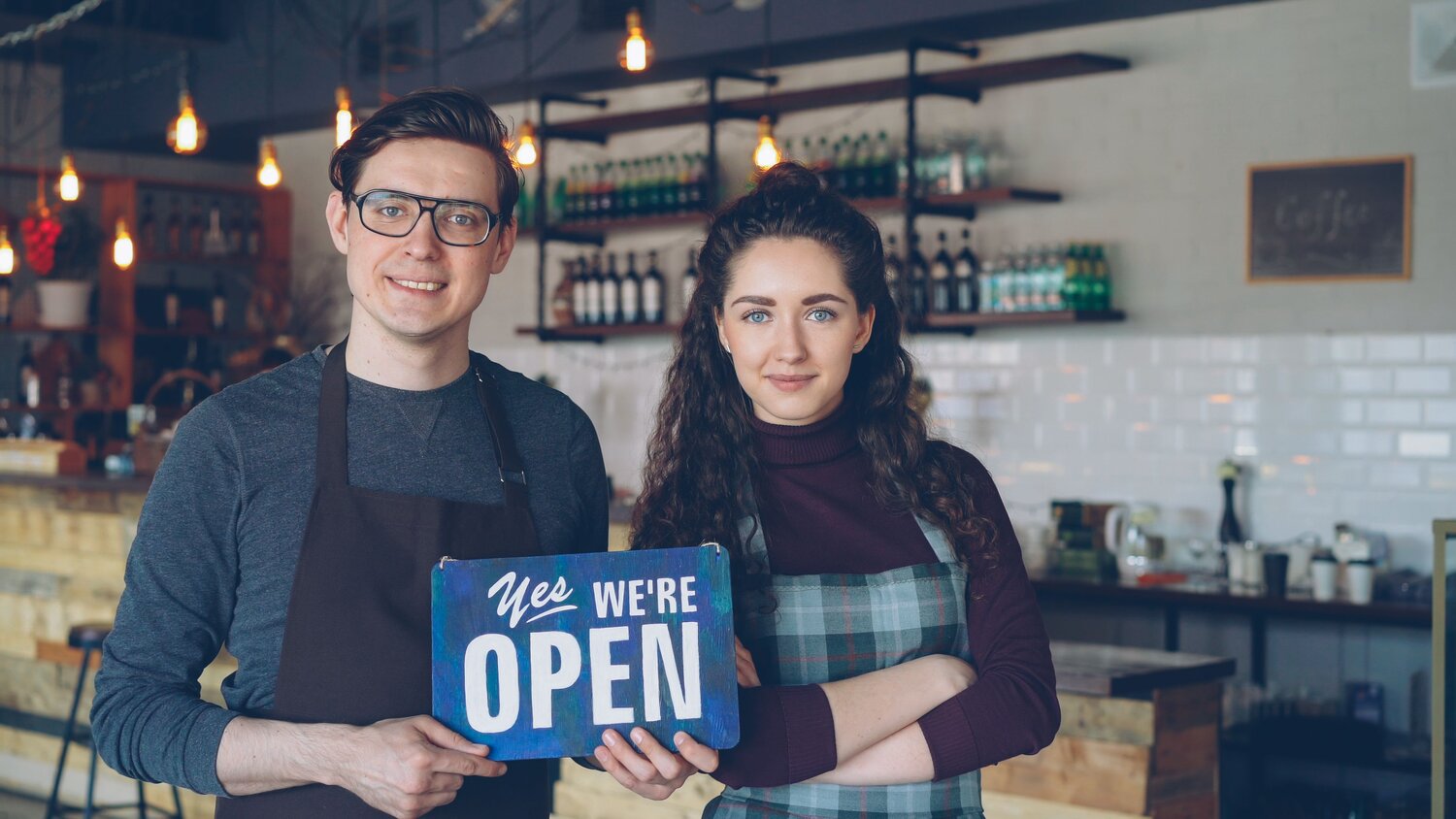 Two small-business owners holding an open sign in their cafe